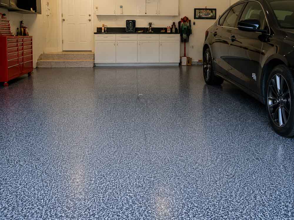 Gray flake epoxy garage floor with parked car and white cabinets